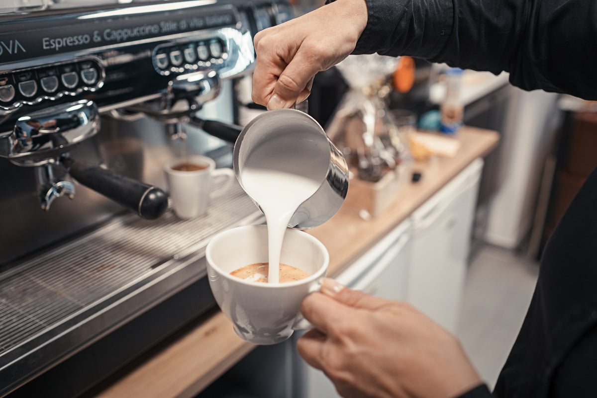 Drei Kaffeetüten von Beans & Friends mit blauen, orangefarbenen und türkisfarbenen Etiketten auf einem Holztisch, daneben eine Tasse Kaffee, Kaffeebohnen und Aromenzutaten.