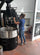 „Kaffeerösterin  Tina in ihrer Produktionshalle, zieht eine Probe während des Röstvorgangs an ihrem großen, schwarzen Röster – präzises Handwerk und Leidenschaft für Kaffeequalität."