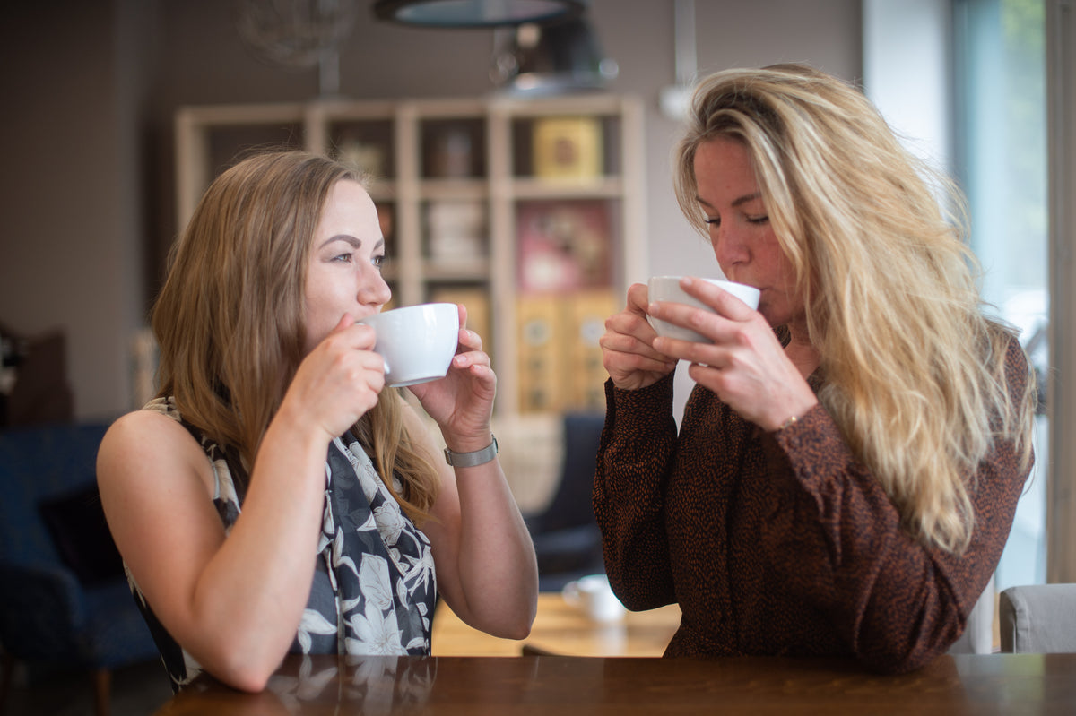 Zwei Frauen sitzen im Beans & Friends Kaffeeladen gemeinsam am Tisch und genießen Kaffee.