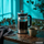 French Press mit frisch zubereitetem Kaffee, Tasse und Kaffeebohnen auf einem Holztisch vor türkisfarbenem Hintergrund.